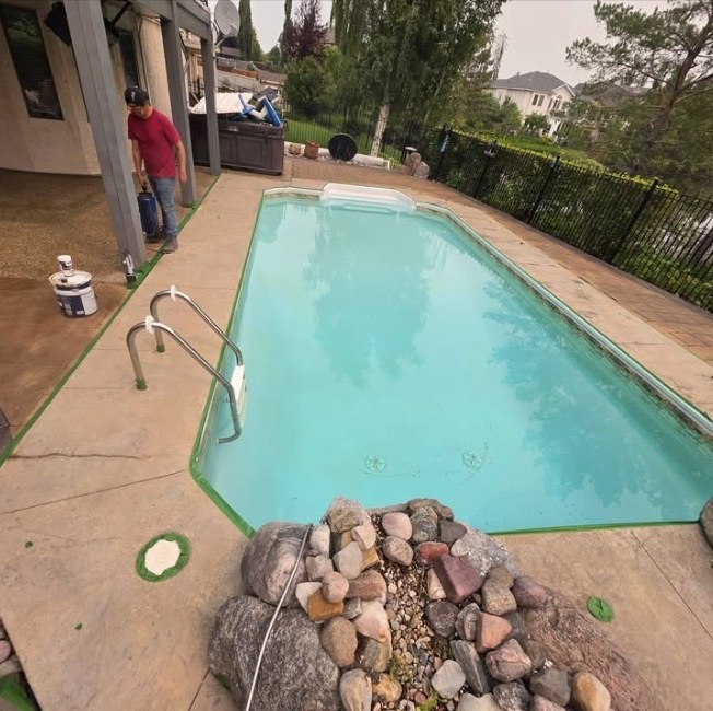 Faded stamped pool deck masked with green tape and prepared for sealing