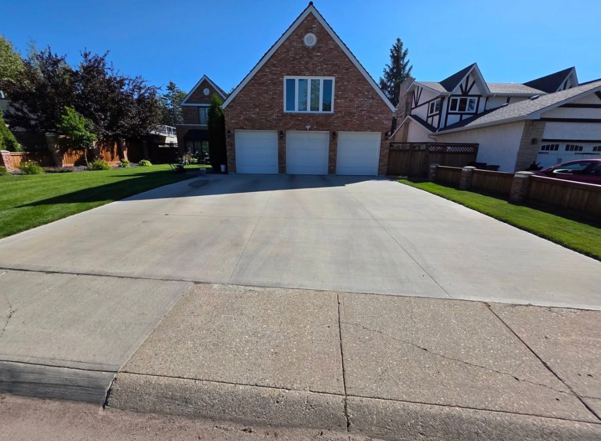 Pale, weathered broom-finish concrete driveway in front of a triple garage before sealing